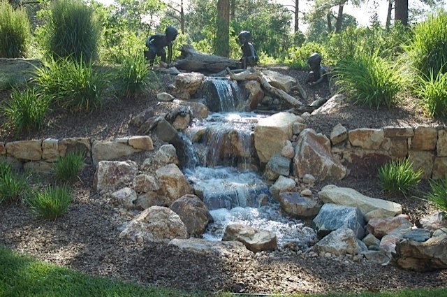 Beautiful bronze statuary accent a pondless waterfall built in this wooded backyard. — Castle Pines, CO.