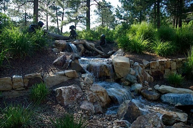 Beautiful bronze statuary accent a pondless waterfall built in this wooded backyard. — Castle Pines, CO.