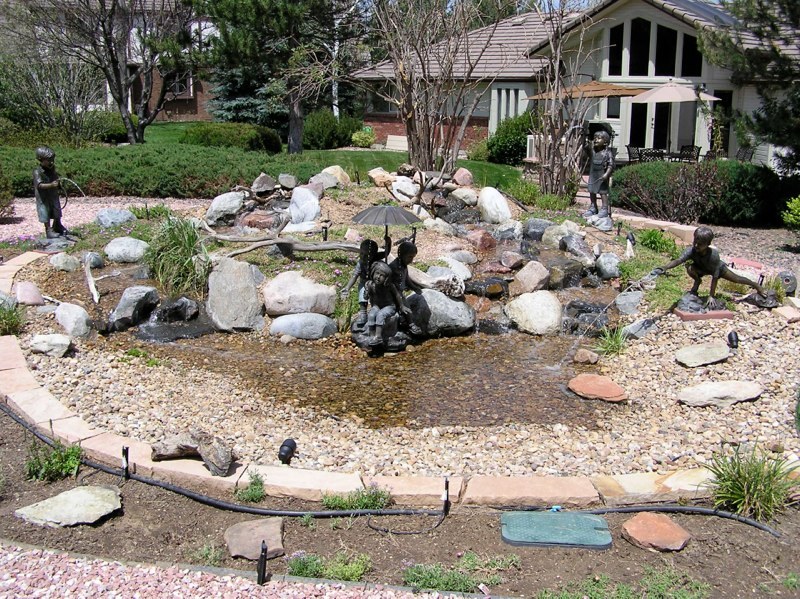 Water loving cherubs surround this pondless water feature right after a devastating Arvada, Colorado hailstorm defoliates the shrubbery and trees.